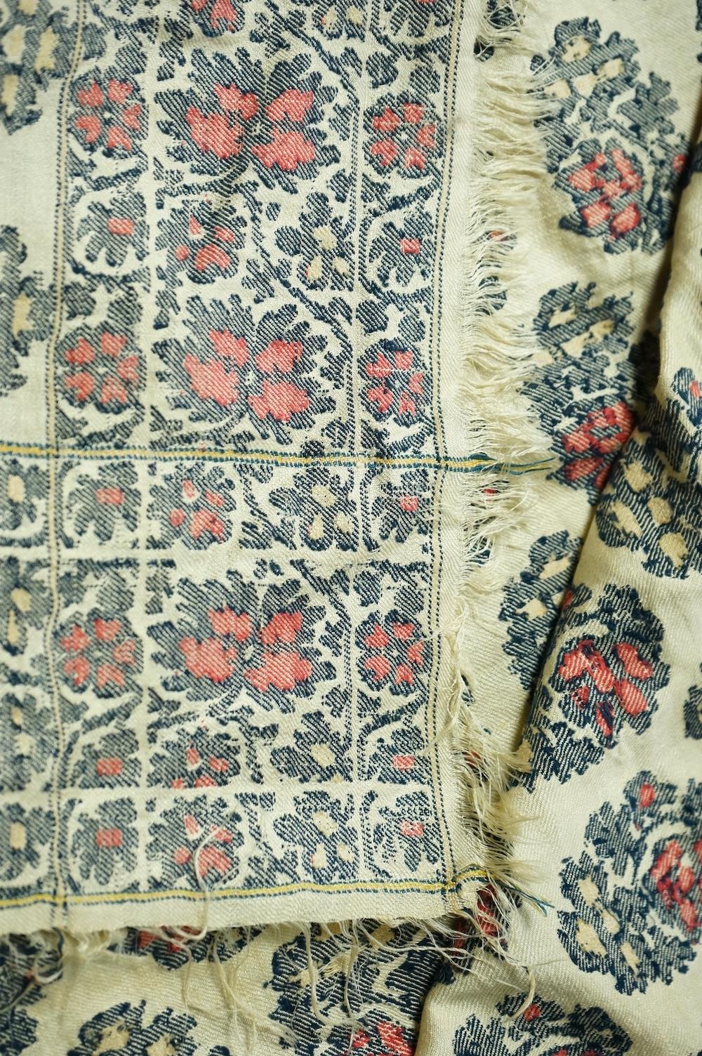 A 19th century silk woven shawl. Woven with a cream silk ground, with indigo, red and yellow, floral stylistic Buta motifs and bordered with three rows of a similar floral vining pattern. The edges fringed. 148cm x 152cm